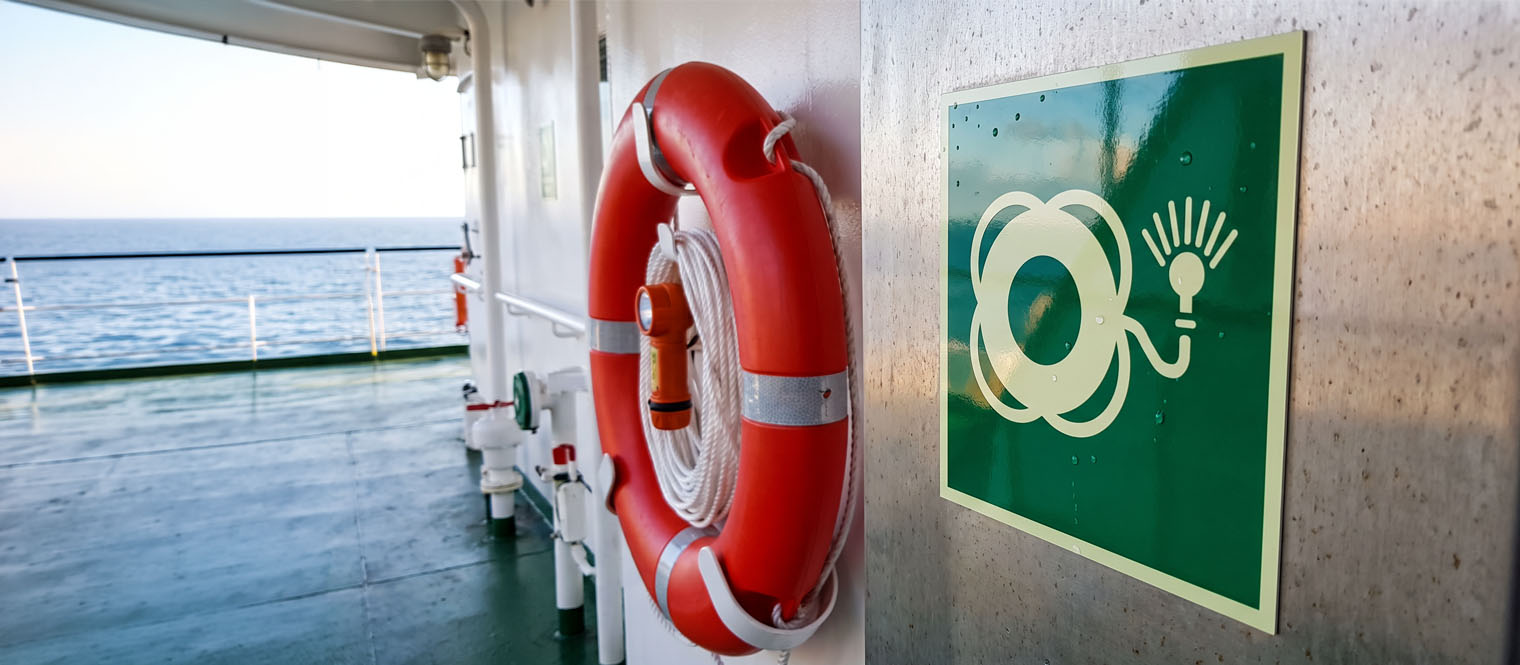 Life-saving appliance signage beside the equipment it identifies on deck, with the equipment in frame.