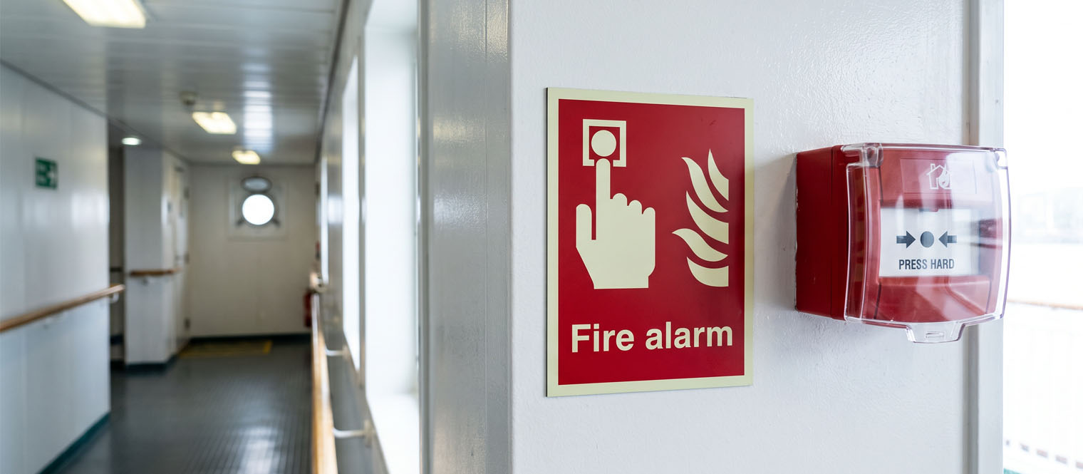 A fire-fighting equipment location sign beside an extinguisher or hose cabinet aboard a vessel.